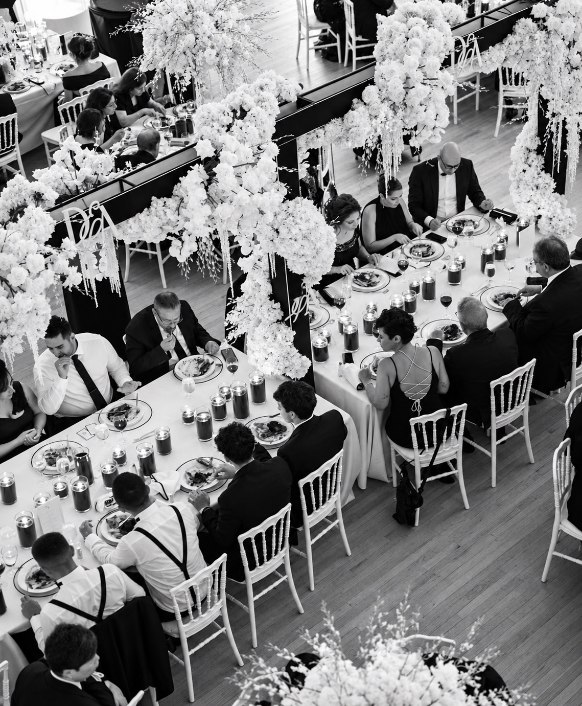 Black and white overhead view of wedding guests dining beneath abundant white floral installations