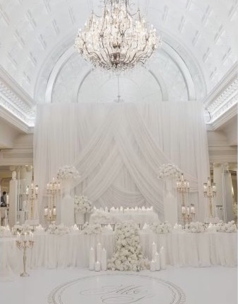 Layered white draping, flowers and candlelight beneath a grand chandelier