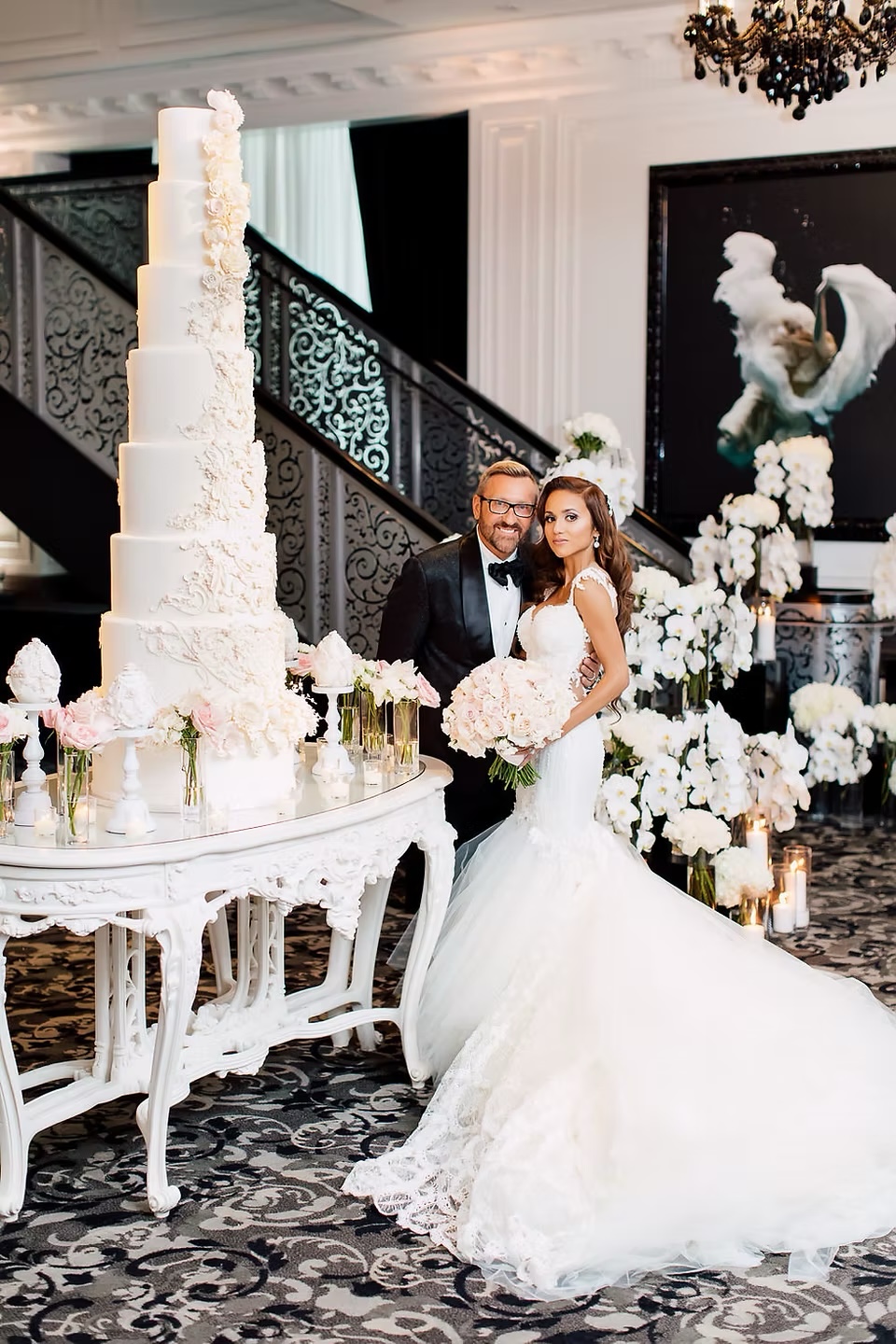 Bride and groom beside a dramatic white cake and floral installation