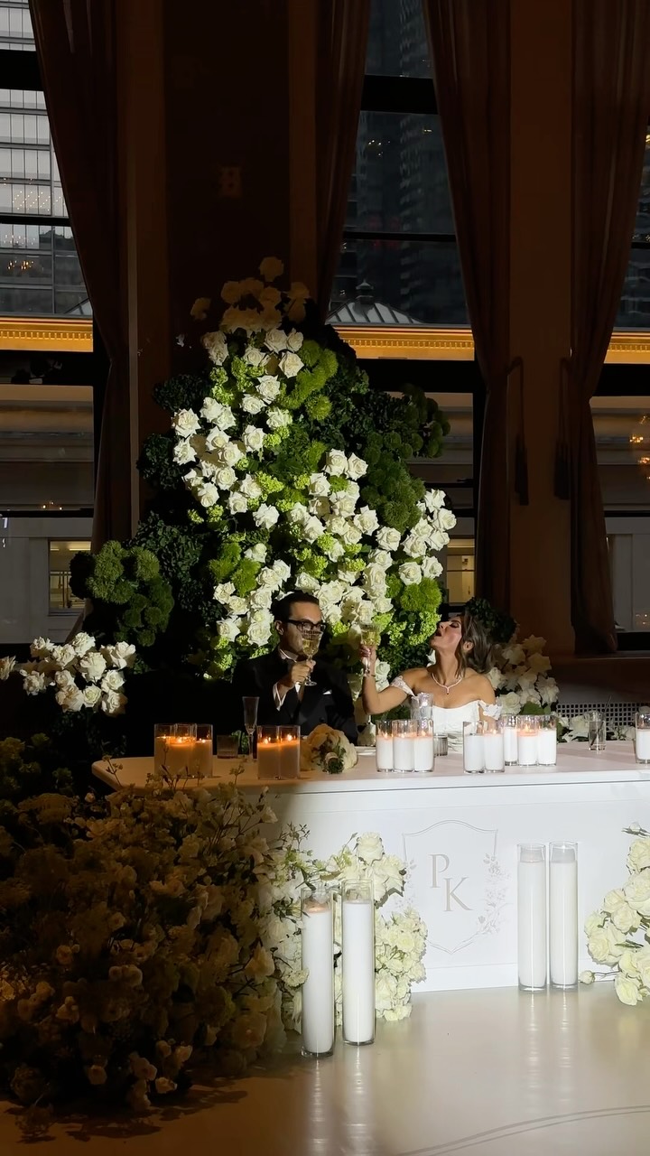 A dramatic candlelit head table backed by sculptural white and green florals