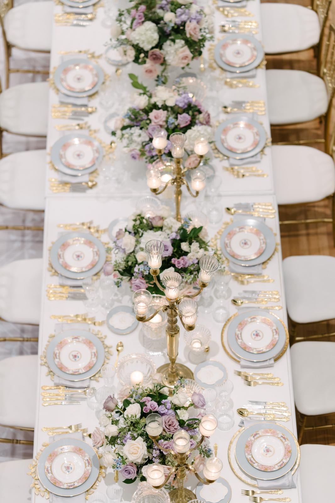 An overhead table setting with heirloom-style china, gold flatware, and lavender flowers