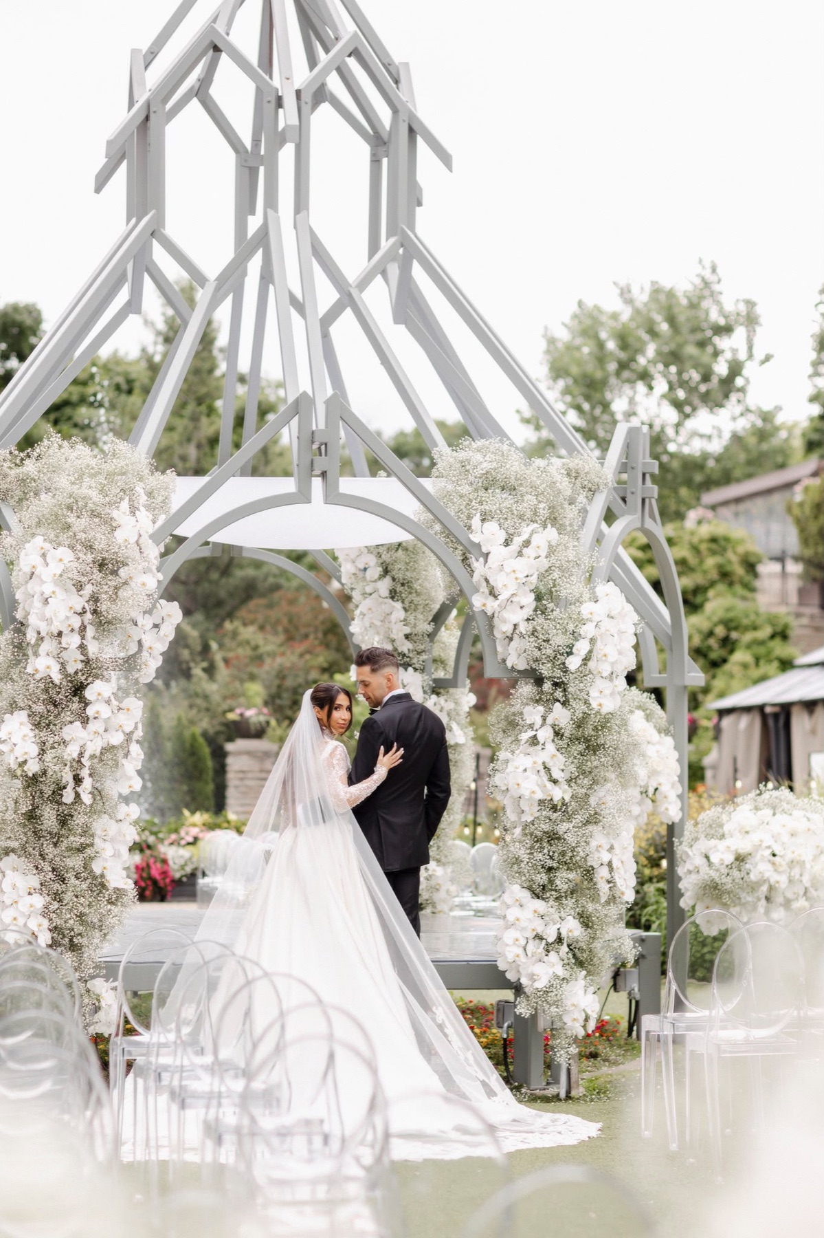 A couple beneath a white orchid ceremony arch in the gardens at Casa Loma, Toronto