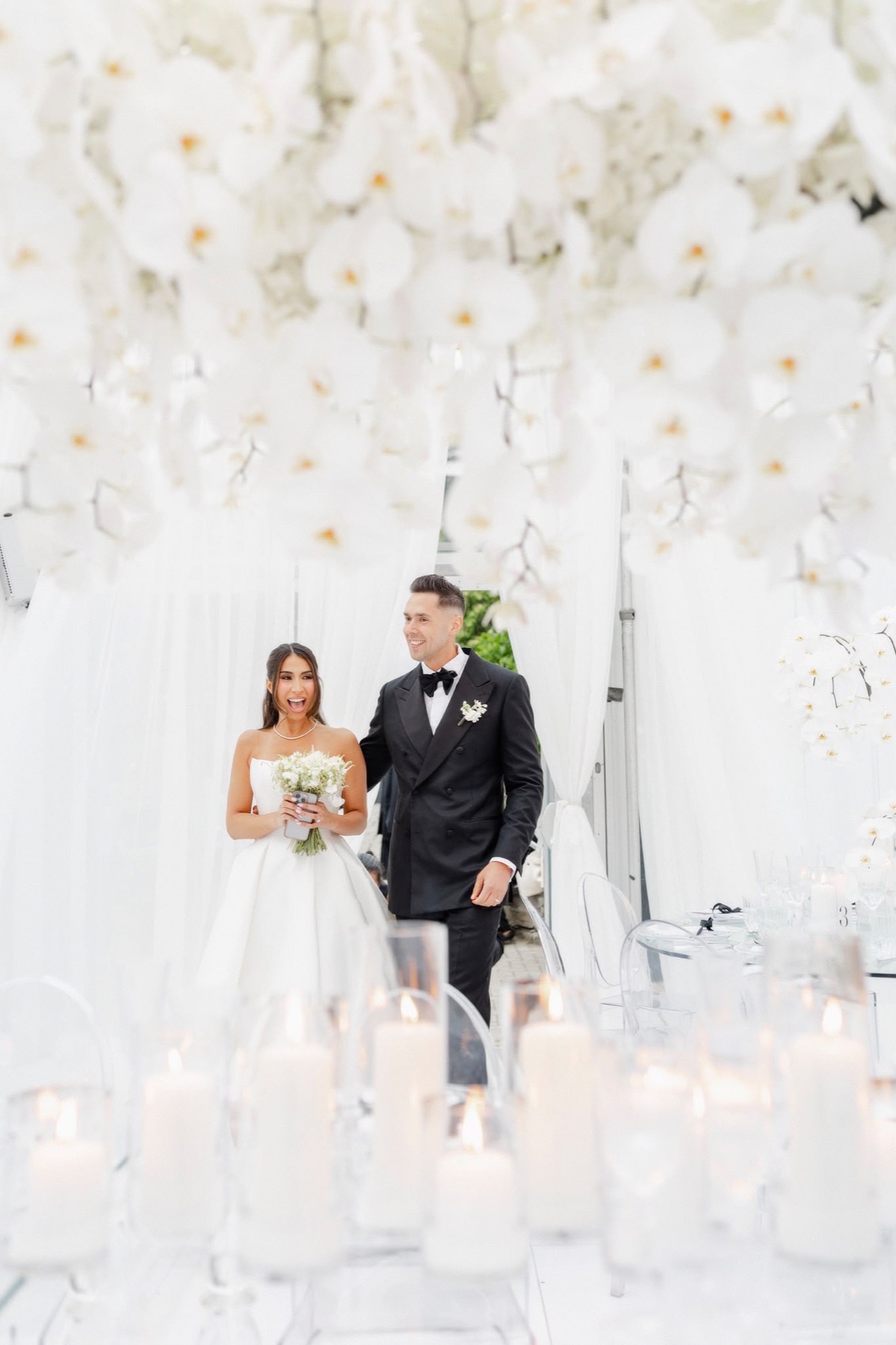 A joyful couple entering a reception beneath suspended white orchids