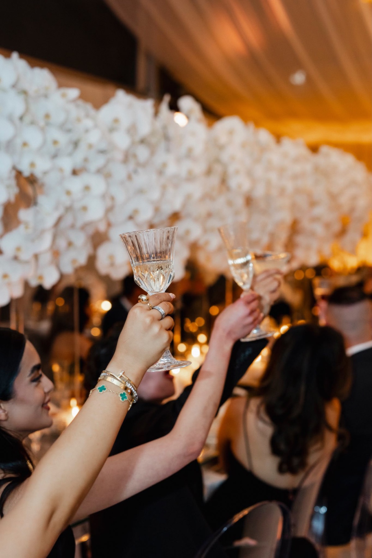 Guests raising crystal glasses beneath a warm orchid canopy
