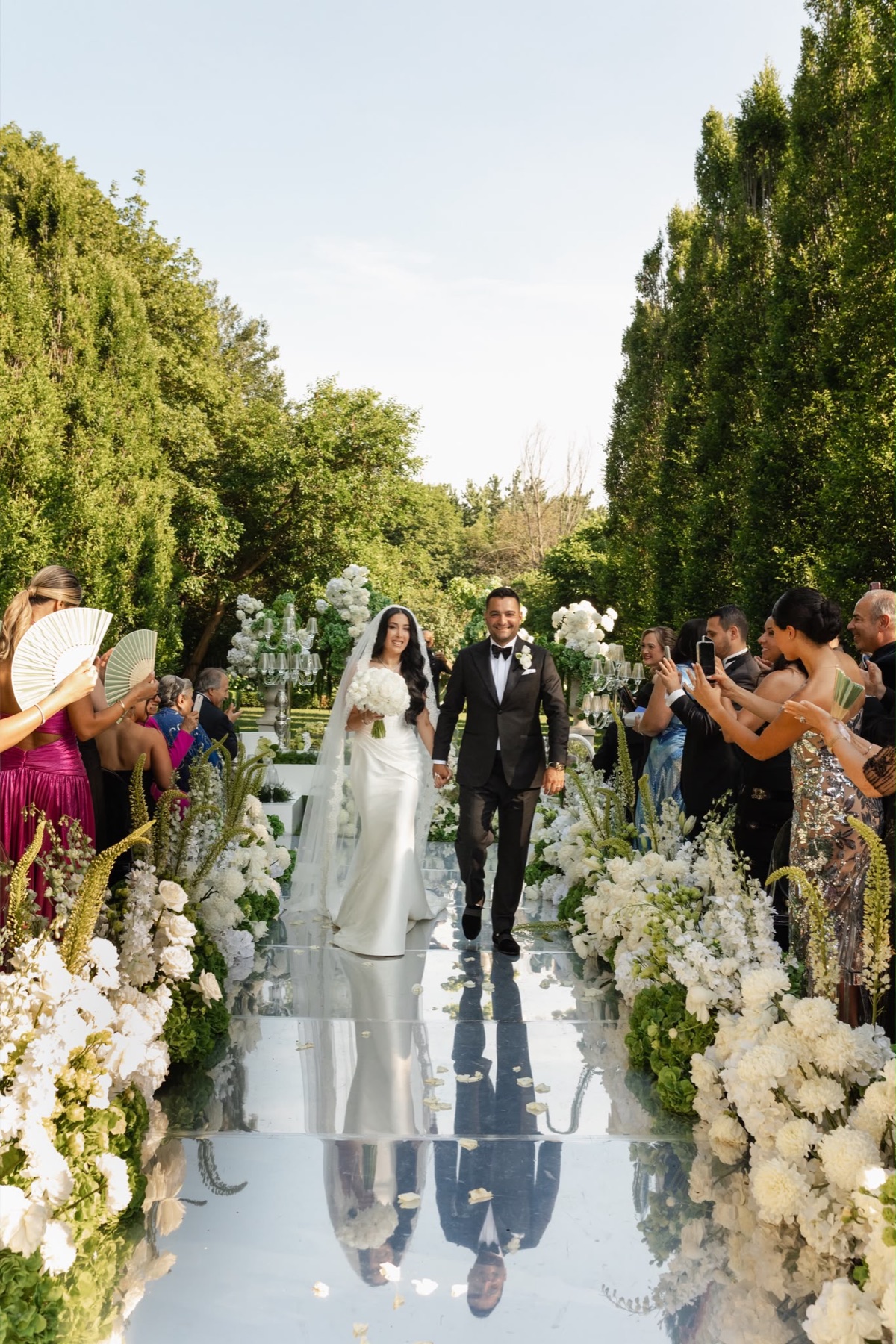 A newly married couple walking down a flower-lined garden aisle