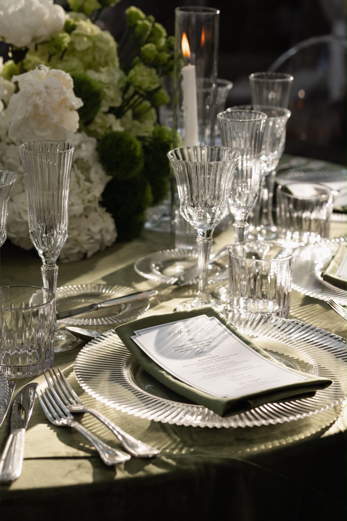Crystal glassware, green linens, and white flowers in afternoon light