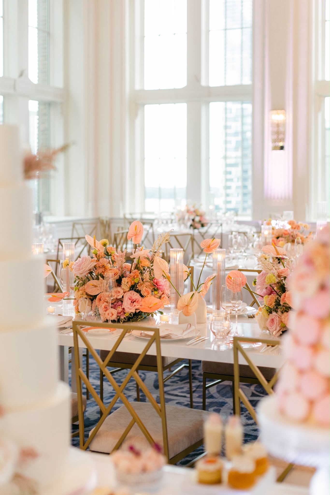 A bright reception room with peach flowers, gold chairs, and tall windows
