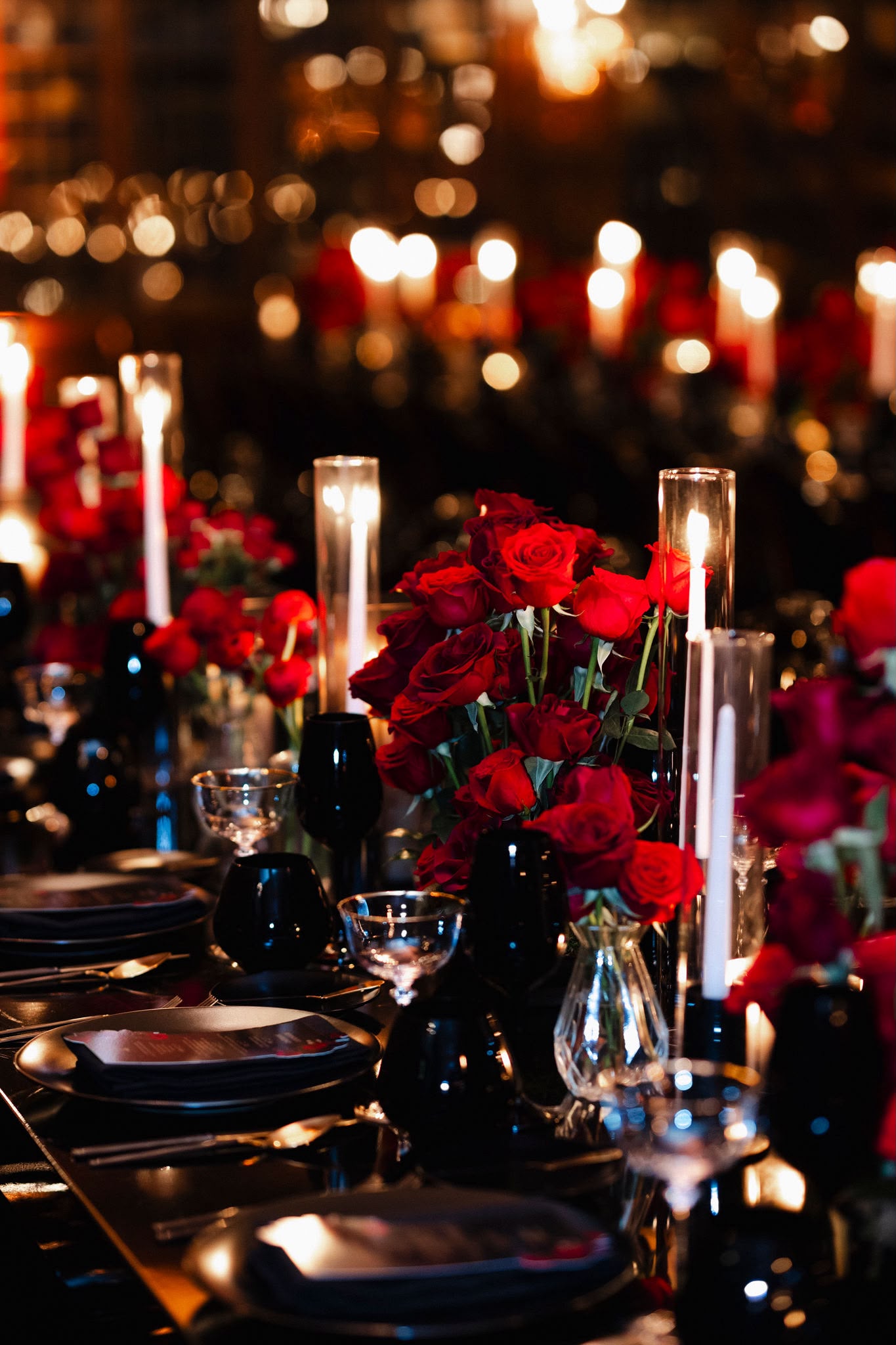 A black reception table layered with red roses, black glassware, and candlelight