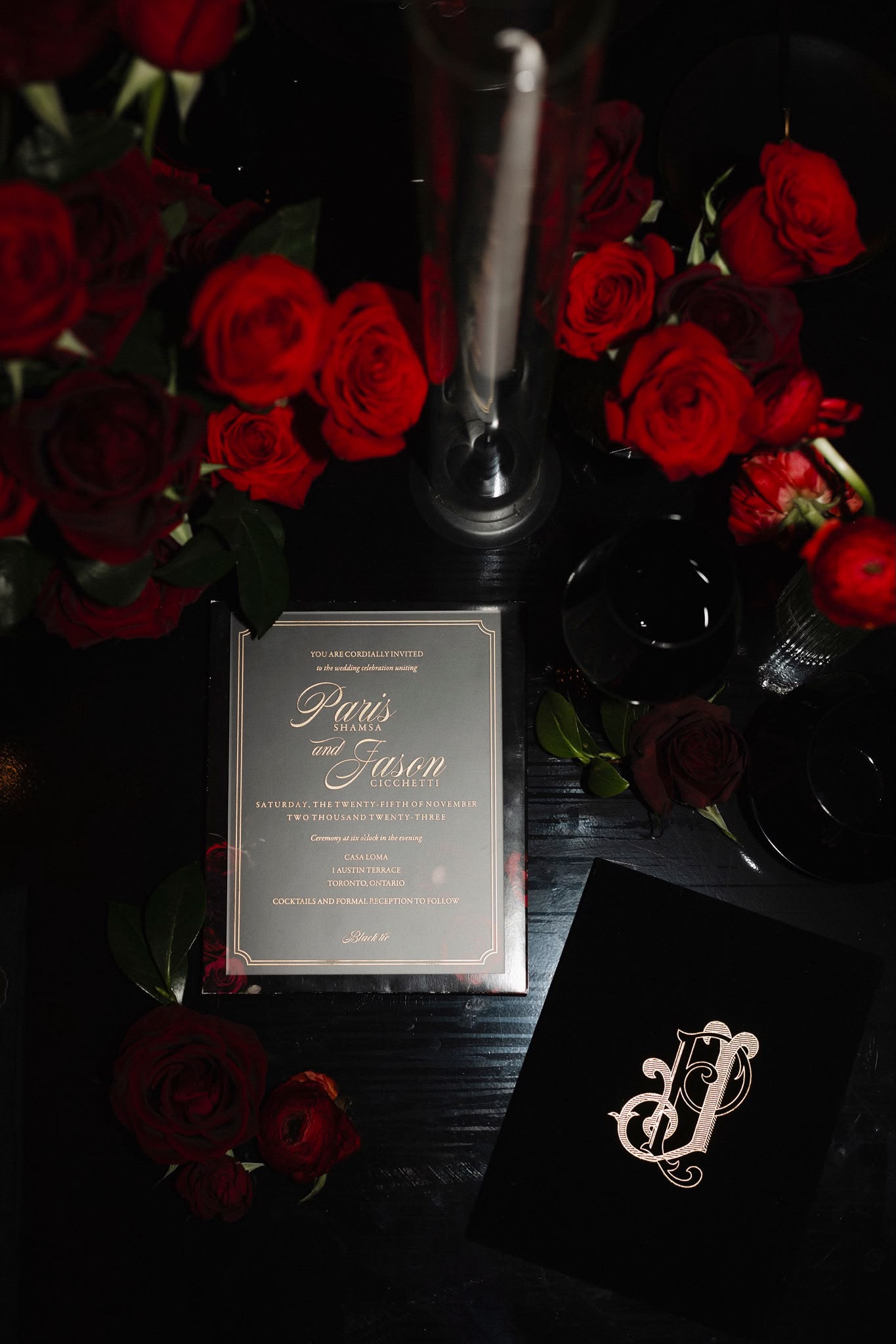 A wedding invitation framed by deep red roses and black place settings
