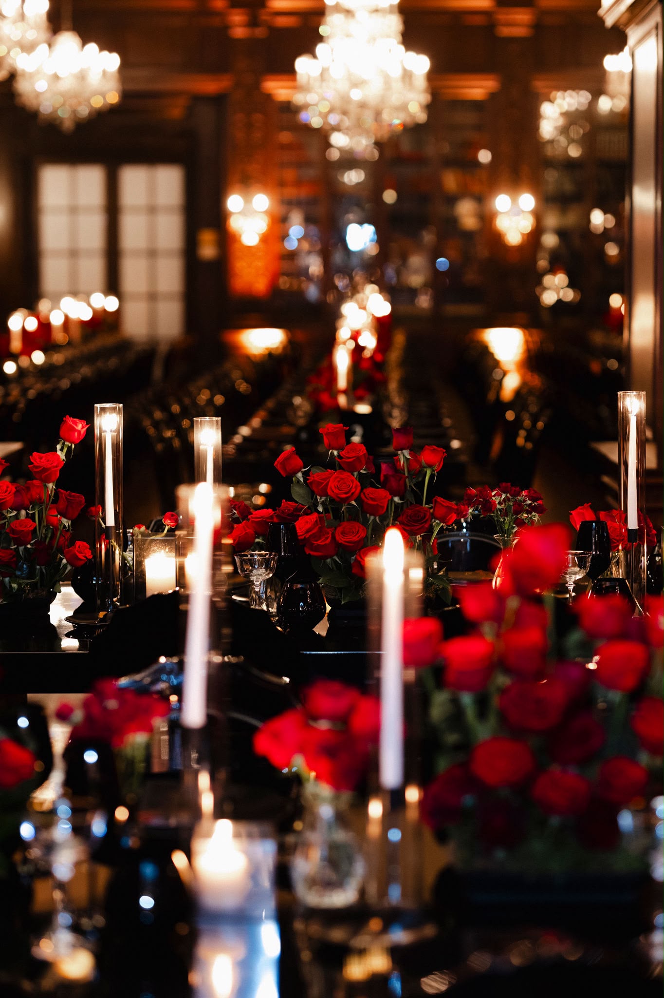 Red roses and taper candles reflected across a glossy black reception table