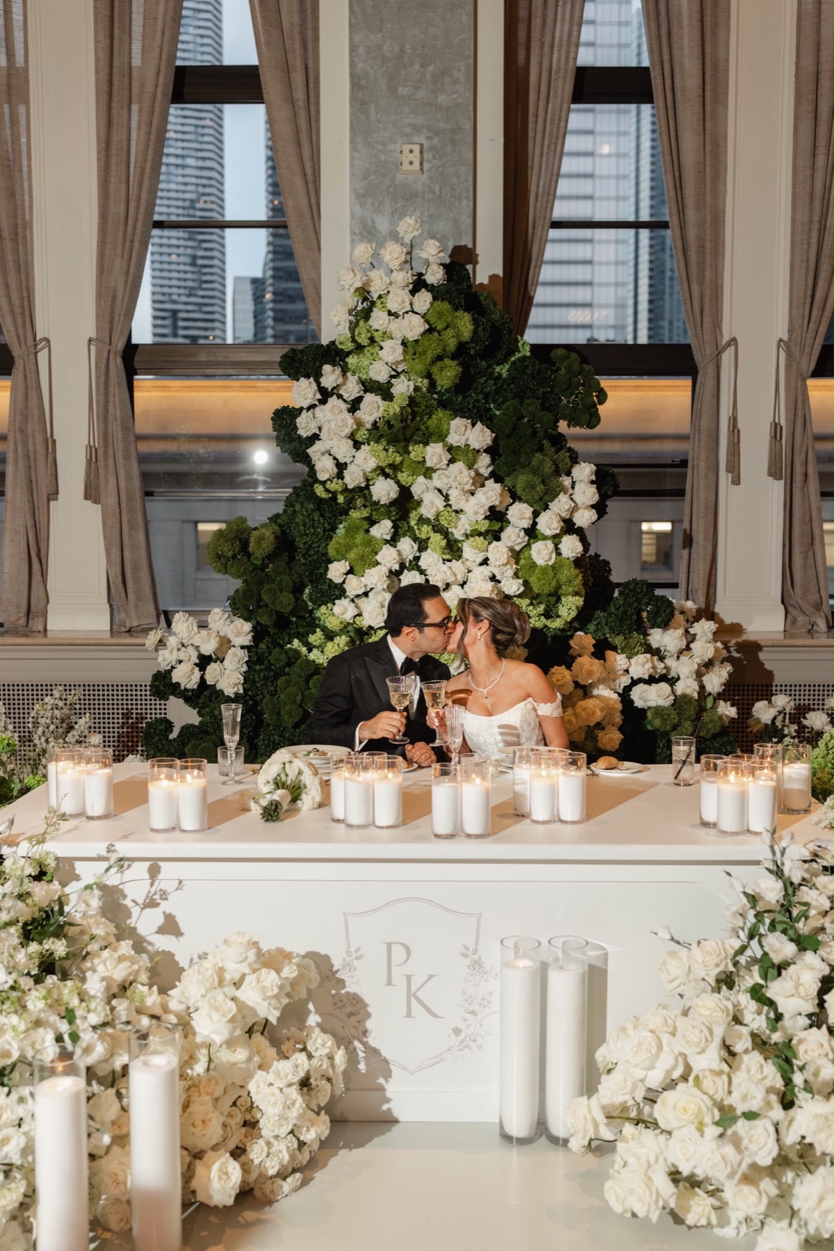 A couple sharing a kiss at a candlelit white and green head table
