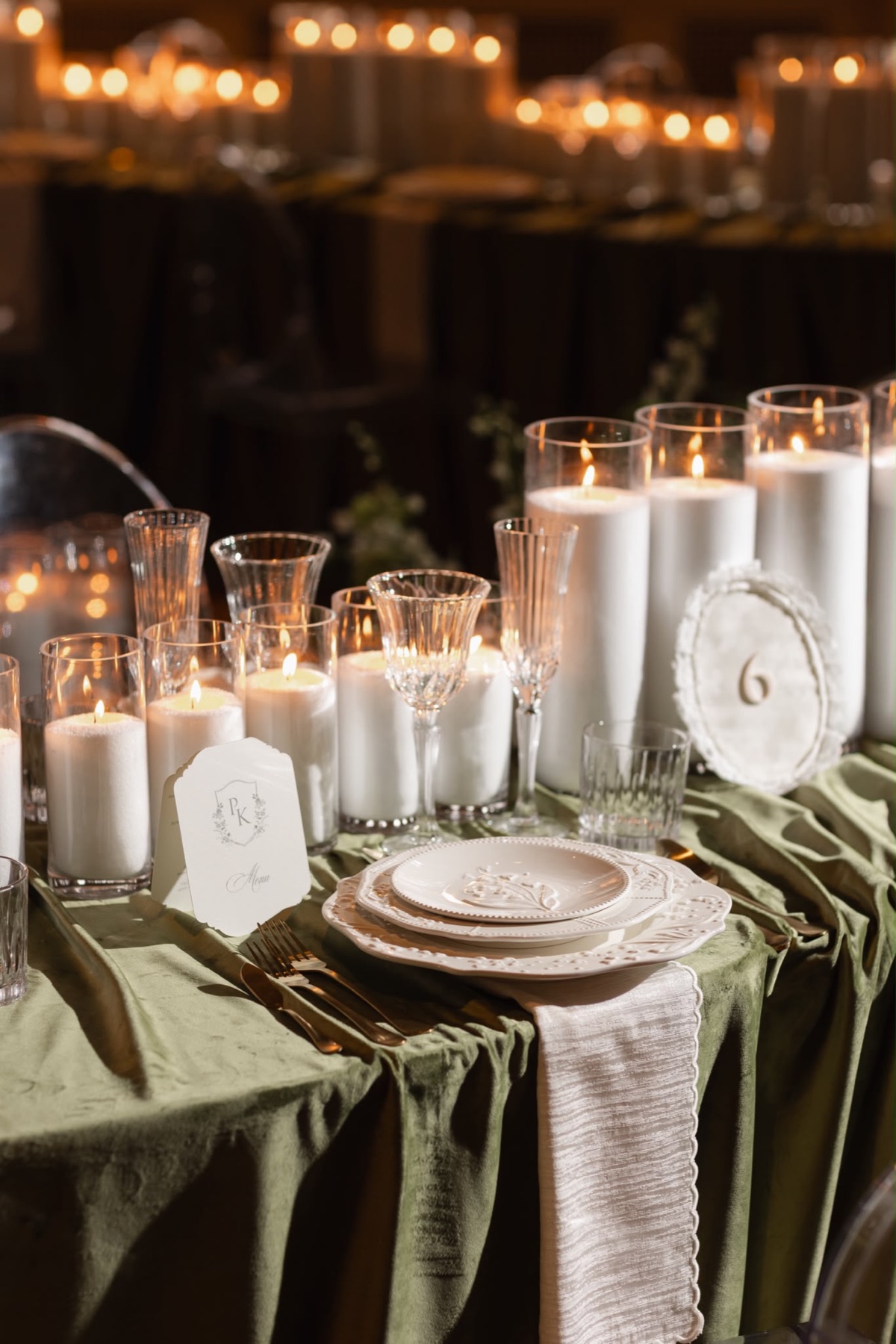 An olive green and white place setting surrounded by candlelight