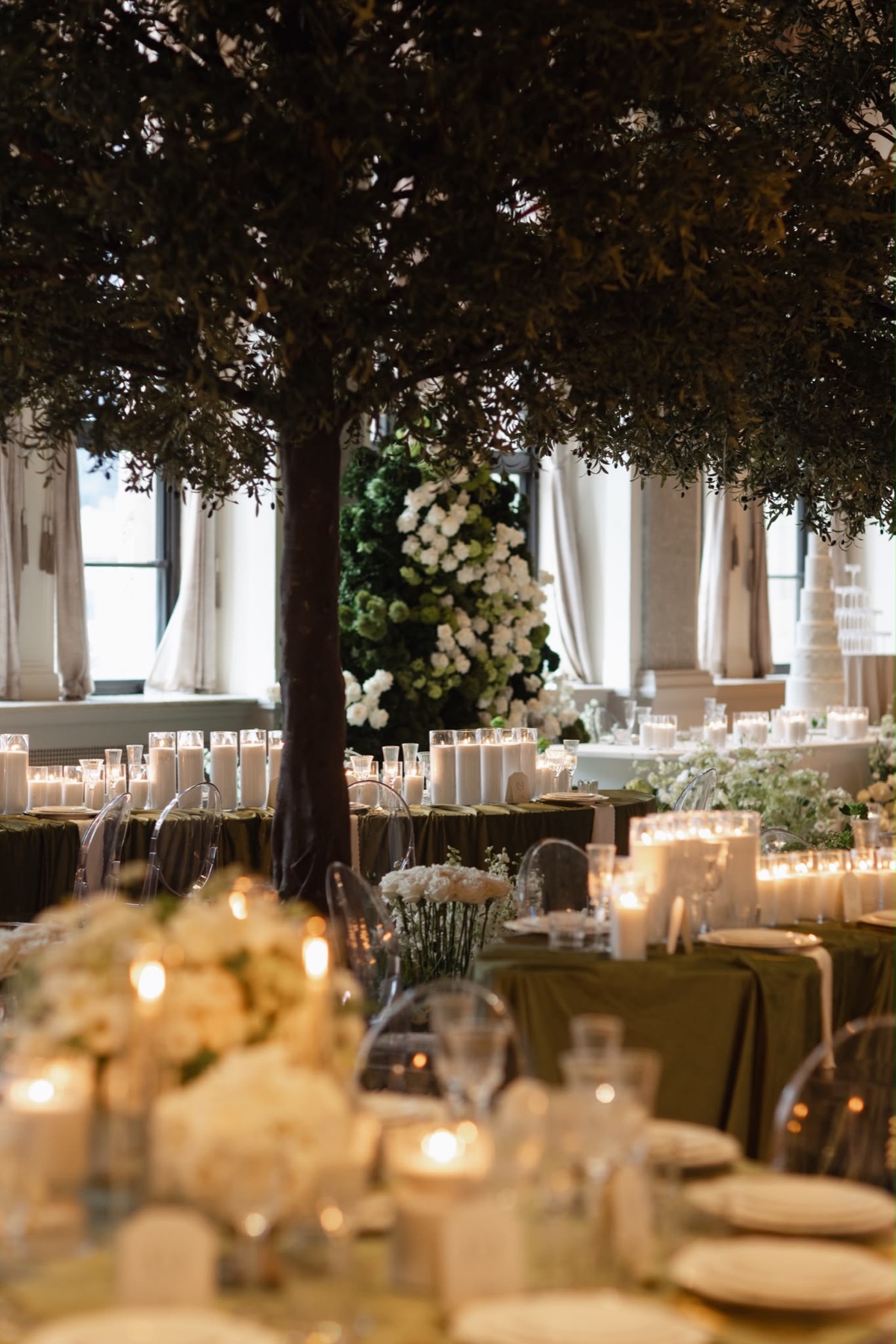 A candlelit ballroom with indoor trees and olive green tables
