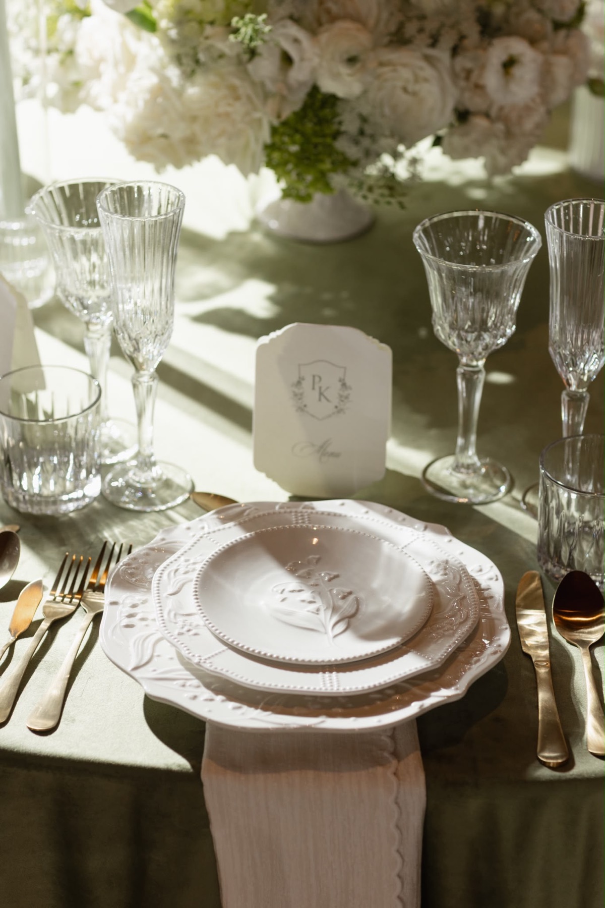 A detailed white place setting with crystal glassware and green linen
