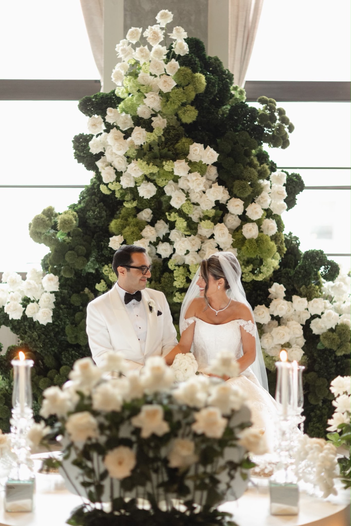 A couple seated before a sculptural green and white floral installation