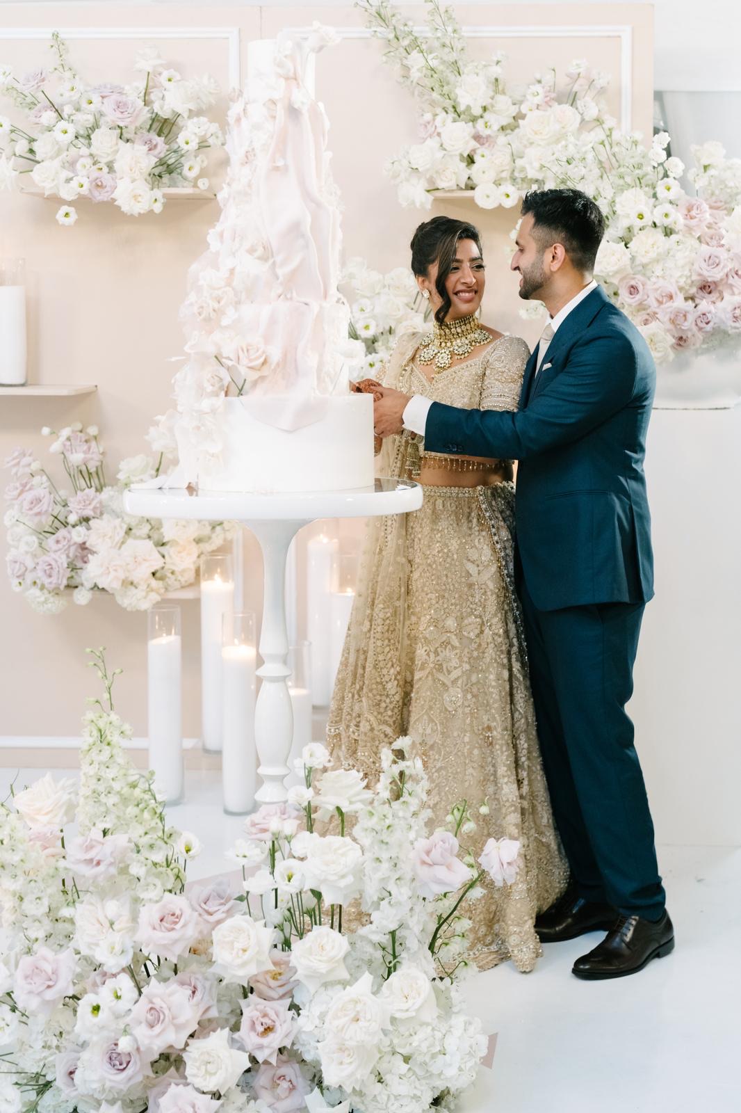 A couple cutting their wedding cake amid blush and white floral design