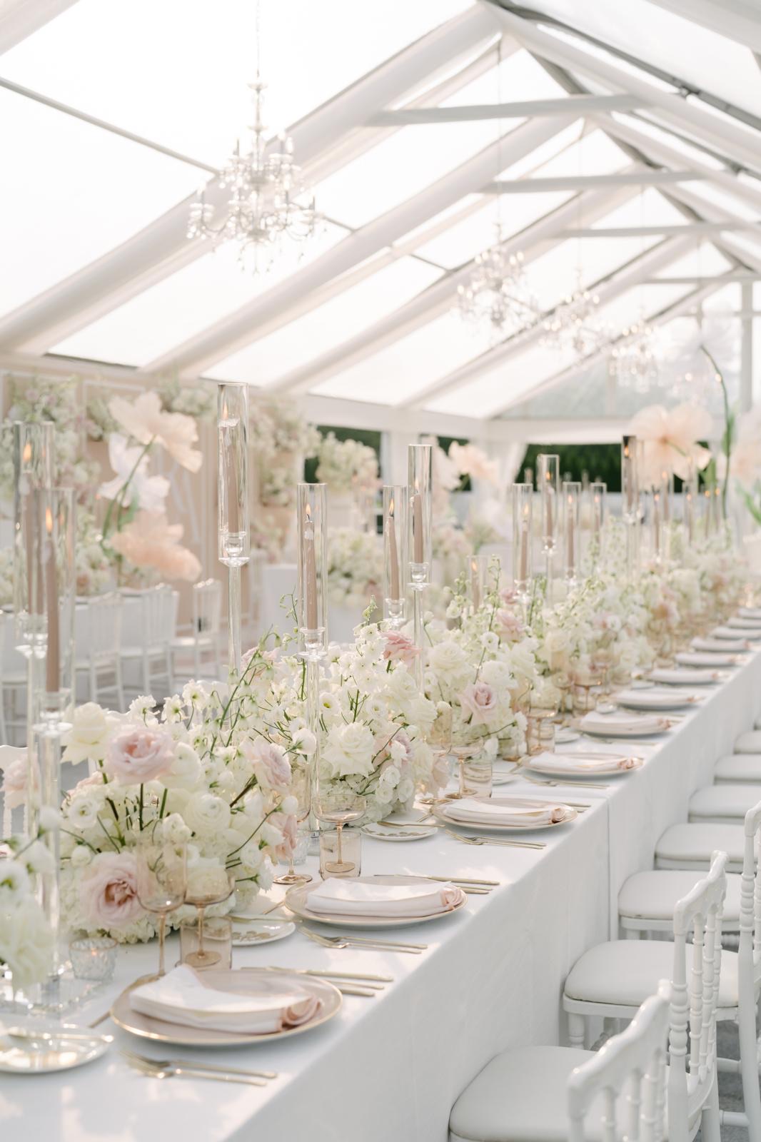 A long reception table layered with blush flowers, crystal candlelight, and white place settings