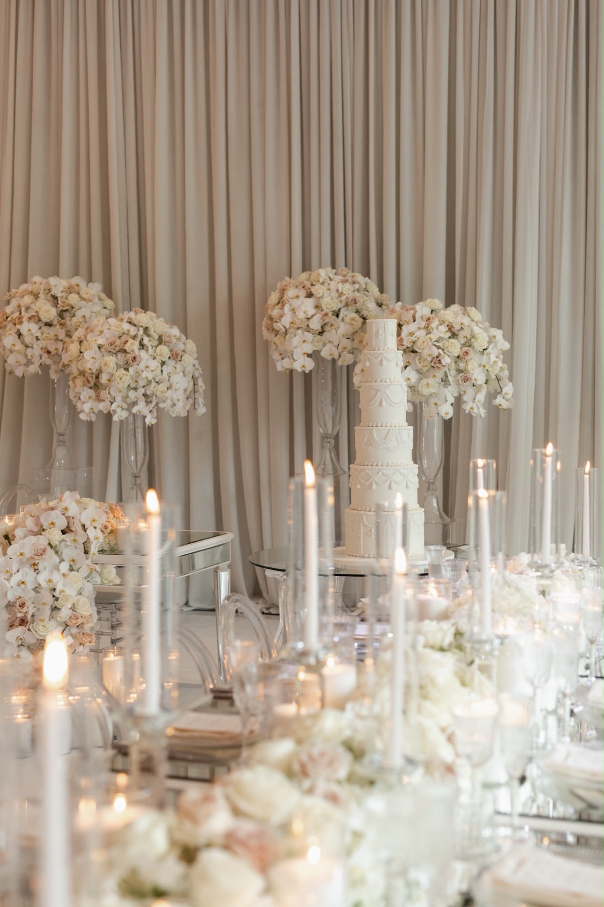 A tall white wedding cake framed by blush flowers and taper candles